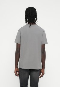 Szara bawełniana koszulka o luźnym kroju, z krótkimi rękawami i okrągłym dekoltem, widoczna od tyłu. Minimalistyczny design, bez wzorów i zdobień.