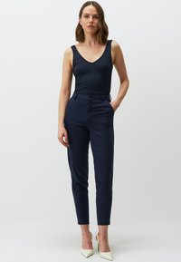Body in raso blu navy a costine con scollatura a V, abbinato a pantaloni blu navy su misura e tacchi color crema. L'outfit presenta una silhouette aderente.