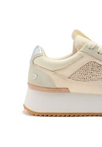 Sneaker beige con una parte superiore in suede e tessuto intrecciato, accento metallico argento sul tallone, suola bianca spessa e suola in gomma marrone chiaro. Dettagli del design testurizzati.