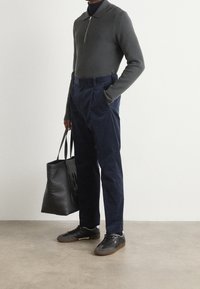 Grå zip-up tröja, marinblå veckade byxor, svarta sneakers med bruna sulor och en svart tote-väska. Släta texturer med en åtsittande silhuett.