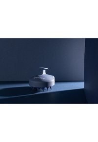 Grå hovedbundsmassager med en rund krop, et topgreb og gummibørster. Indeholder præget tekst og kaster en tydelig skygge.