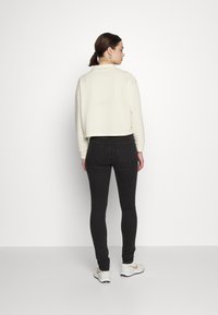 Sweatshirt curto creme com decote redondo, combinado com jeans skinny pretos. O conjunto apresenta mangas longas e um design simples.