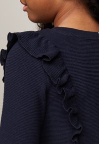 Maglione a coste navy con un inaspettato accento arricciato lungo la spalla. Il tessuto ha una consistenza morbida e una leggera elasticità, per un comfort maggiore.