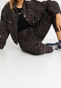 Conjunto de chaqueta y pantalones negros con un patrón floral multicolor, cierre de botón en la chaqueta y zapatos casuales azules. Ajuste cómodo y tela texturizada.