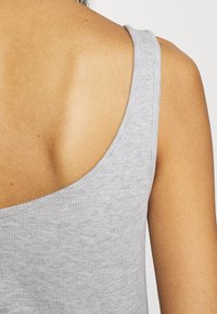 Gray ribbed tank top with wide shoulder straps and a deep scoop back. Made of a soft, stretchy material with a slightly textured finish.
