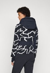 Doppellagige Jacke in Marineblau mit weißem abstraktem Muster. Verfügt über eine taillierte Passform, eine verstellbare Kapuze und gerippte Bündchen für zusätzliche Wärme.