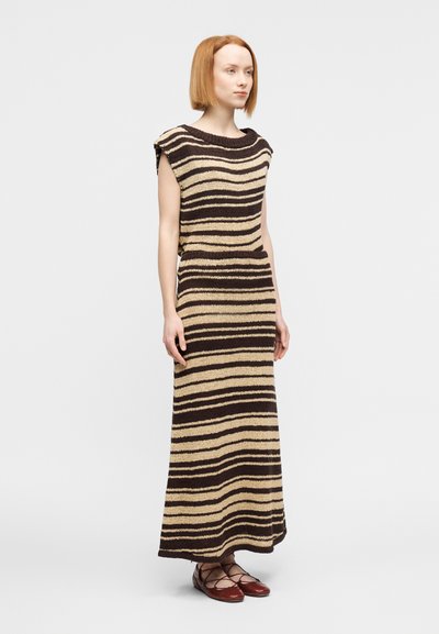 Πλεκτό μάξι φόρεμα με οριζόντιες ρίγες σε μπεζ και σκούρο καφέ. Χοντρή κλωστή, φαρδιά μανίκια και στρογγυλός λαιμός. Συνδυασμένο με κόκκινα φλατ παπούτσια.