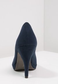 Zapato de tacón alto azul marino con punta afilada y textura de ante suave. Presenta un tacón delgado y un forro interior suave. Sin herrajes ni acentos visibles.