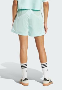 Pantalones cortos deportivos verde menta con una cinturilla elástica, combinados con calcetines rayados blancos y zapatos con acentos negros. Tejido suave y ligero.