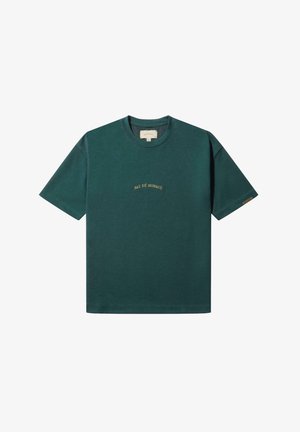 Temno zelena bombažna majica s kratkimi rokavi in okroglim izrezom. Na prsih je v zlati vezenini napisan 'PAS DÉ MONACO'. Čist, minimalističen dizajn.
