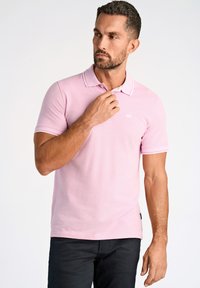 Polo de color rosa claro con tela texturizada, cuello blanco y bordes de las mangas con dos finas rayas. Logo sutil en el pecho.