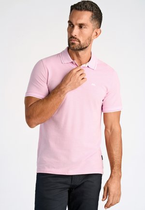 Ljusrosa polo shirt med ett texturerat tyg, vit krage och ärmslumpar som har två tunna ränder. Diskret logotyp på bröstet.