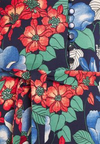 Tessuto floreale con fiori rossi e blu, foglie verdi, una cintura coordinata e una fila di piccoli bottoni blu tondi su sfondo navy.