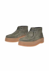 Pattini alla caviglia in pelle verde oliva con finitura testurizzata, caratterizzati da una robusta suola in gomma scanalata e un midsole marrone a contrasto.
