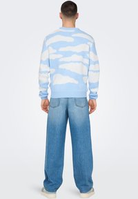 Lyseblå strikket sweater med hvid sky-mønster, ribbede manchetter og kant. Båret med vide, falmede jeans.