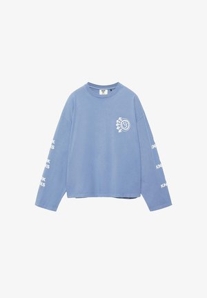 Svetlomodrá dlhá košeľa s bielym kruhovým logom na hrudi a bielym textom "KNWK" opakujúcim sa na oboch rukávoch.