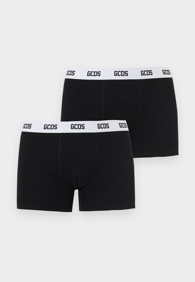 Δύο μαύρα μποξεράκια με λευκές ελαστικές ζώνες στη μέση, που φέρουν επαναλαμβανόμενο λογότυπο GCDS σε μαύρα γράμματα.