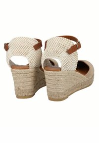Sandali wedge beige con tomaia in tessuto intrecciato, cinturino alla caviglia e suola intermedia in juta naturale. Presentano un elegante dettaglio in pelle marrone vicino alla fibbia.