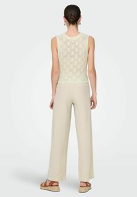 Top de punto verde claro con patrón de encaje, combinado con pantalones de pierna ancha beige y sandalias de esparto, creando una textura en capas y un estilo relajado.