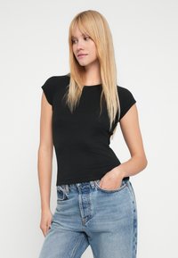 Μαύρο τοπ με κοντά μανίκια και εφαρμοστή γραμμή, με στρογγυλή λαιμόκοψη, φτιαγμένο από μαλακό, ελαστικό υλικό· συνδυασμένο με ψηλόμεσα μπλε τζιν.