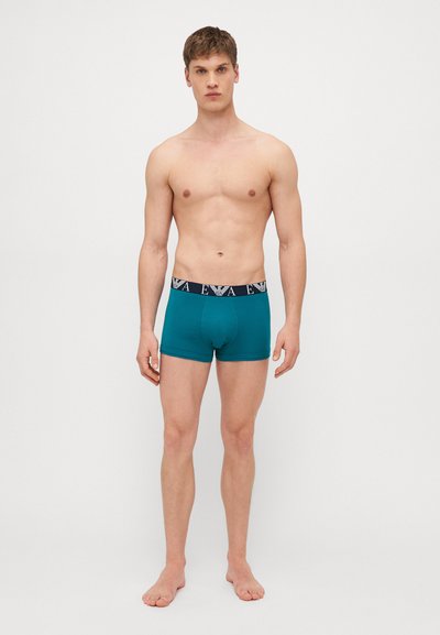 Boxer da uomo teal con una cintura con logo navy, realizzati in tessuto morbido, con un design aderente e una tasca frontale.