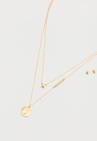 Collana a strati in oro con un pendente circolare e un accento rettangolare, e due catene delicate con borchie triangolari. Orecchini abbinati.