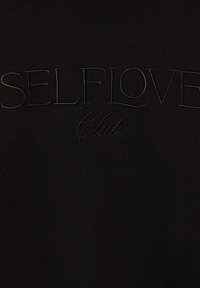 Felpa nera con testo ricamato "SELFLOVE" in un font grassetto e "Club" in uno stile corsivo, caratterizzata da una texture liscia e morbida.