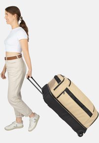 Beige und schwarze Stoff-Reisetasche mit Rollen, ausgestattet mit zwei Griffen, Reißverschlusstaschen und glatten Rollen für einfachen Transport.