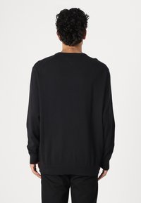 Maglione nero a maniche lunghe con scollatura tonda, polsini e orlo a coste. Texture liscia con vestibilità comoda. La vista posteriore mostra la semplicità del design.