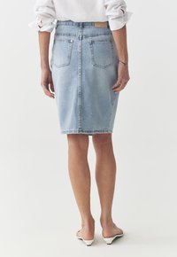 Lichtgewassen denim rok met een aansluitende vorm, knielengte, voorzien van twee achterzakken en zichtbare stiksels. Glad textuur en minimalistisch ontwerp.