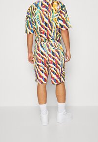 Ensemble chemise à manches courtes et short à motifs multicolores. Présente des lignes ondulées audacieuses en rouge, jaune, vert et bleu sur une base blanche.