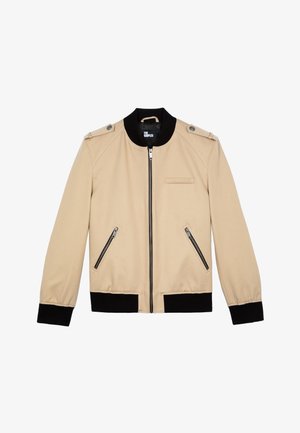 Beige Bomberjacke mit schwarzen gerippten Bündchen und Saum; verfügt über einen Frontreißverschluss, zwei Reißverschlusstaschen und Schulterklappen.