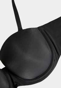 Coque de soutien-gorge rembourrée noire avec bretelle ajustable et tissu lisse, montrant un gros plan sur les détails de la couture et de la texture.