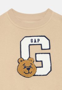 Felpa beige con la scritta in blu "G" e "GAP", arricchita da una faccina di orso ricamata in brown sotto la lettera.