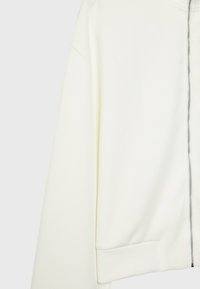 Sudadera blanca con cremallera, que presenta una textura suave, un corte relajado y puños acanalados. Destaca la cremallera de metal en la parte delantera.