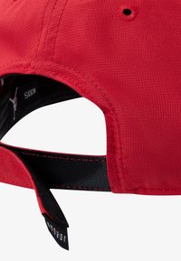 Cappellino in tessuto rosso con superficie strutturata, cinturino nero regolabile sul retro e una piccola etichetta con il nome del marchio.