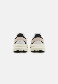 Two athletic shoes featuring a mesh upper in white with light pink and black accents, a thick cream sole, and a textured rear for support.