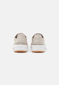 Světlé béžové tenisky s síťovinou, elastickými pásky a bílými podrážkami. Mají texturovaný povrch a nízkoprofilový design.