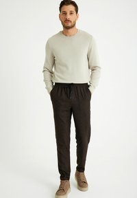 Beige gebreide trui gecombineerd met donkerbruine geruite joggingbroek, voorzien van een elastische tailleband, trekkoord en een taps toelopende pasvorm. Casual schoenen.