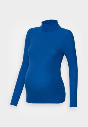 Haut de grossesse bleu côtelé à manches longues avec col roulé et fronces latérales, présenté sur fond blanc.