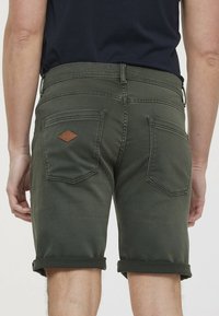 Shorts en coton vert avec des ourlets roulés, dotés d'une taille cousue et d'un écusson en cuir marron sur la poche arrière. Design classique à cinq poches.