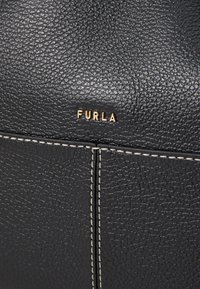 Zwart textuurleer handtas met een gouden "FURLA" logo, met crèmekleurige stiksel en een gladde vormgeving.