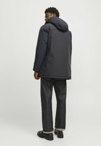 Marine isoleret jakke med hætte, der har en glat tekstur og sidelommer, parret med mørk denim jeans og sorte sko.