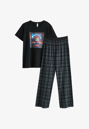 Dreng stående barfodet iført en sort t-shirt med en kat, der spiller videospil, og mørke ternede pyjamasbukser mod en ensfarvet baggrund.