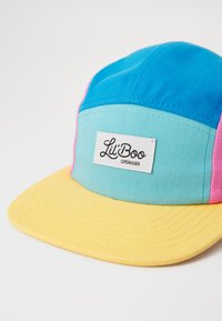 Bunt gefärbte Kappe mit einem blauen und türkisfarbenen Oberteil, rosa Akzenten und einem gelben Schirm. Auffälliges Etikett mit der Aufschrift "Lil' Boo Copenhagen."