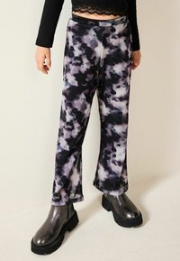 Czarno-purpurowe spodnie typu tie-dye o szerokich nogawkach, wykonane z miękkiego materiału o gładkiej teksturze, zestawione z błyszczącymi czarnymi botkami za kostkę.