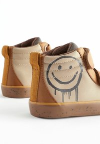Scarpe alte marroni e beige con design a faccina sorridente, tessuto texture e suole in gomma con motivi a macchie e cinturini in Velcro.