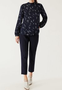 Blusa navy con stampa floreale, maniche lunghe a palloncino, scollatura alta; abbinata a pantaloni navy su misura e scarpe con tacco quadrato grigio chiaro.