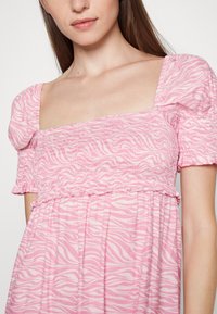 Vestido rosa claro com decote quadrado e mangas bufantes. Apresenta um corpete franzido e uma saia solta e fluida com padrão de zebra.