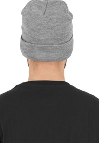 Grå strikket beanie med brettet mansjett, med et teksturert mønster, kombinert med en svart t-skjorte som er synlig nedenfor.